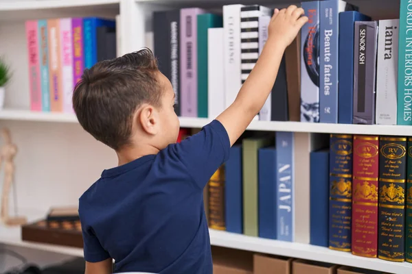 図書館学校で棚の本を持っている愛らしいヒスパニック系の幼児 — ストック写真