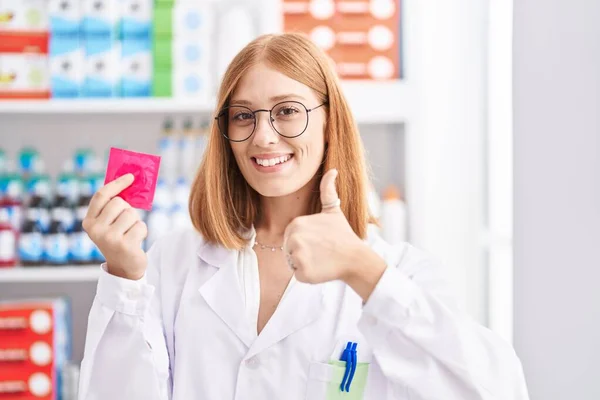 Young Redhead Woman Working Pharmacy Drugstore Holding Condom Smiling Happy — Zdjęcie stockowe