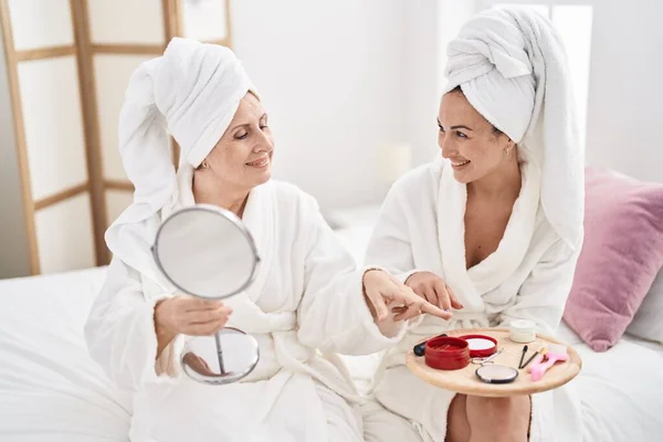 Mother and daughter wearing bathrobe applying skin lotion treatment at bedroom