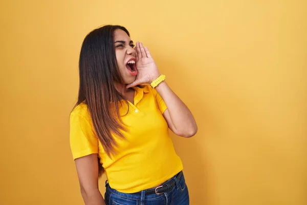 若いアラブ人の女性は黄色の背景に叫んで立って大声で口の上に手で横に叫んでいる コミュニケーションの概念 — ストック写真