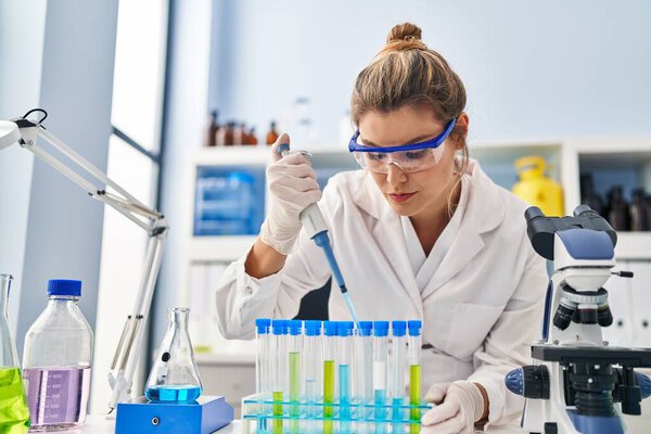 Young blonde woman wearing scientist uniform using pipette at laboratory
