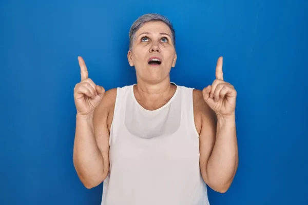 Mujer Caucásica Mediana Edad Pie Sobre Fondo Azul Asombrada Sorprendida —  Fotos de Stock