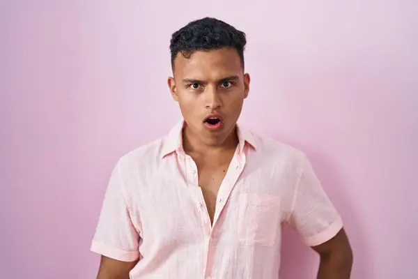 衝撃的な顔でピンクの背景の上に立って若いヒスパニック系の男 懐疑的で皮肉を探して オープン口で驚いて — ストック写真