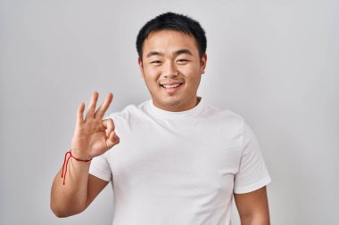 Young chinese man standing over white background showing and pointing up with fingers number three while smiling confident and happy. 