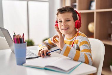 Young caucasian kid doing homework at home doing ok sign with fingers, smiling friendly gesturing excellent symbol 