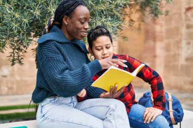 African american mother and son smiling confident reading book at park