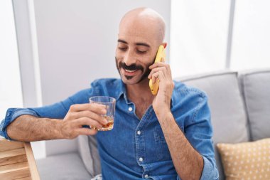 Genç İspanyol adam akıllı telefonda konuşuyor. Evde viski içiyor.