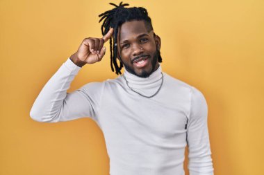 Sarı arka planda balıkçı yaka kazak giyen Afrikalı bir adam gülümseyerek tek parmağıyla, harika bir fikir ya da düşünceyle, iyi bir hafızaya sahip. 