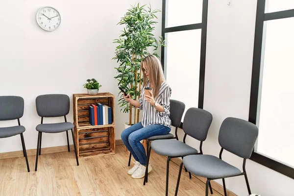 Young chinese woman using smartphone sitting on chair at waiting room