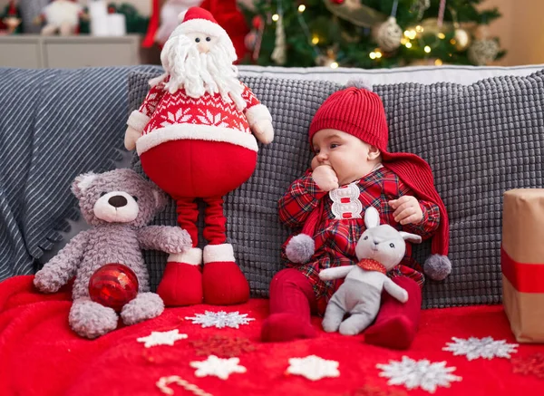 可爱的高加索婴儿吸吮着手指坐在家里圣诞树旁的沙发上 — 图库照片