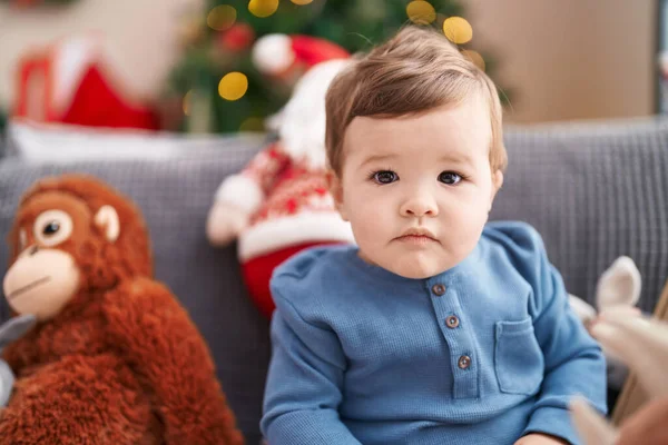 愛らしいCaucasian赤ん坊座っています上のソファによってクリスマスツリーとともにリラックスした表現で家 — ストック写真