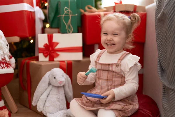 愛らしいです白人女の子遊びますプレートとフォークおもちゃで床に座っていますクリスマスツリーによってホーム — ストック写真