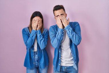 Young hispanic couple standing over pink background rubbing eyes for fatigue and headache, sleepy and tired expression. vision problem 