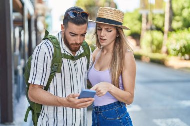 Man and woman tourist couple using smartphone with serious expression at street