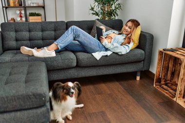 Beyaz bir kadın dokunmatik ped kullanıyor. Evdeki kanepede yatıyor.