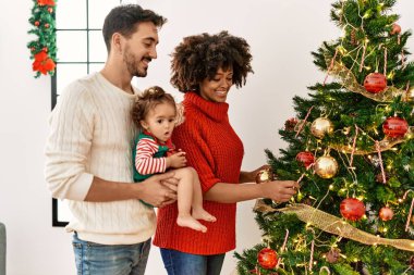 Couple and daughter smiling confident decorating christmas tree at home
