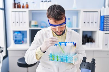 Laboratuvarda deney tüpü tutan bilim adamı üniforması giyen İspanyol genç adam.