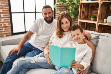 Family reading book sitting on sofa at home
