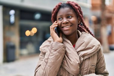 Afro-Amerikalı kadın gülümsüyor. Akıllı telefondan konuşuyor.