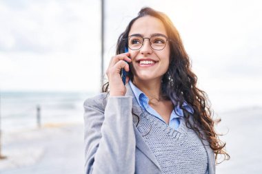 Genç İspanyol kadın yönetici deniz kenarında akıllı telefondan konuşuyor.