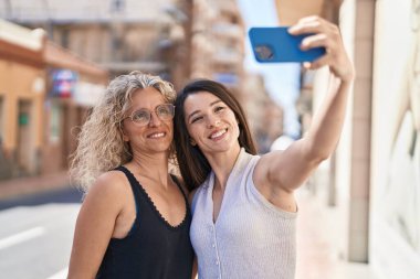 İki kadın anne ve kız sokakta akıllı telefonla selfie çekiyorlar.