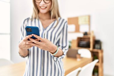 Ofiste akıllı telefon kullanan, kendinden emin gülümseyen genç Çinli kadın.