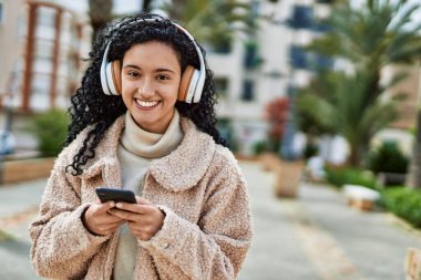 Genç İspanyol kadın parkta akıllı telefon kullanarak gülümsüyor.