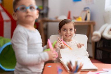 Adorable girl and boy sitting on table cutting paper at kindergarten