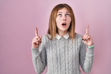 Pembe arka planda duran güzel kadın şaşırmış ve şaşırmıştı. Parmaklarıyla işaret ediyor ve kollarını kaldırıyordu.. 