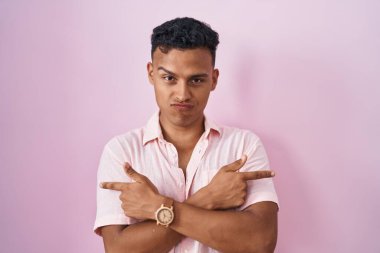 Young hispanic man standing over pink background pointing to both sides with fingers, different direction disagree 