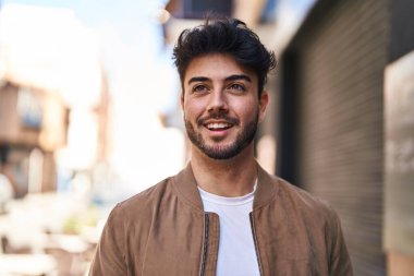 Young hispanic man smiling confident looking to the side at street