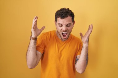 Sarı arka planda duran genç İspanyol adam başarı için deli ve çılgınlığı kutluyor kollarını kaldırmış ve gözlerini kapatmış heyecanla bağırıyor. Kazanan konsept 