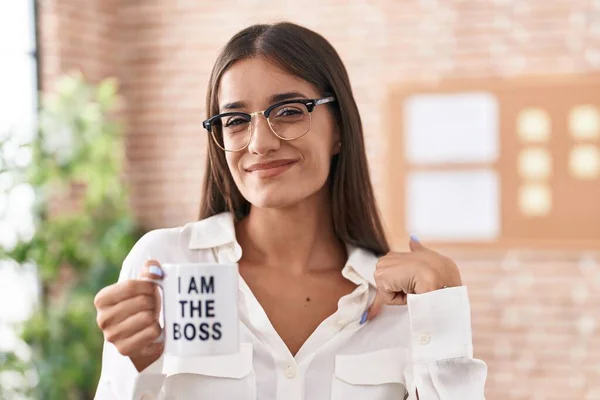 Young brunette woman drinking from i am the boss coffee cup pointing finger to one self smiling happy and proud