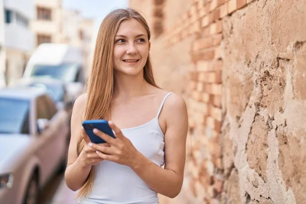 若い白人女性が路上でスマートフォンを使って自信を持って笑っています — ストック写真