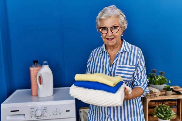 シニア白髪の女性が自信を持って洗濯室で折り畳まれた服を保持笑顔 — ストック写真