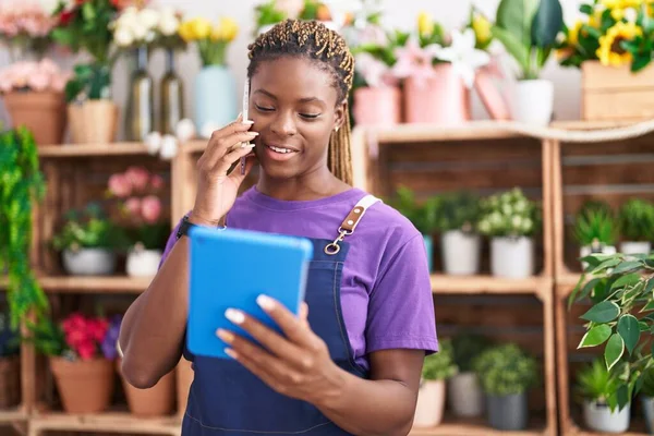 African american woman florist talking on smartphone using touchpad at florist