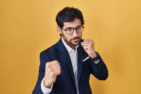Handsome latin man standing over yellow background ready to fight with fist defense gesture, angry and upset face, afraid of problem