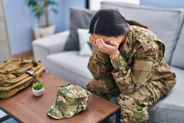 Young hispanic woman army soldier depressed sitting on sofa at home