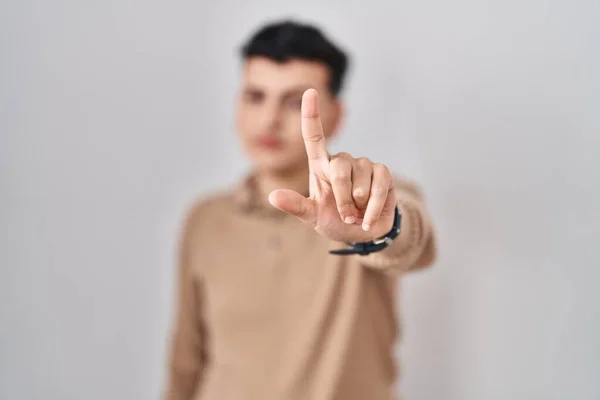 Non binary person standing over isolated background pointing with finger up and angry expression, showing no gesture