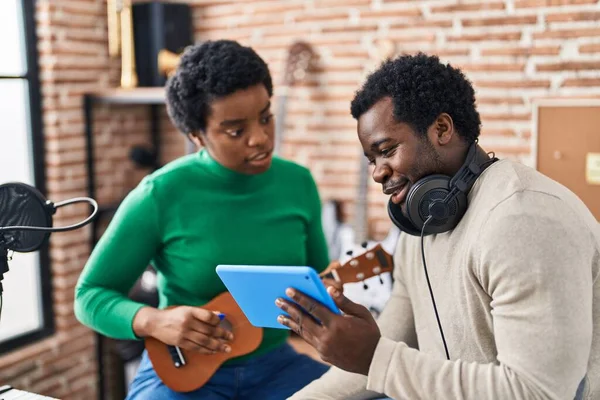 African american man and woman music group using touchpad playing ukelele at music studio