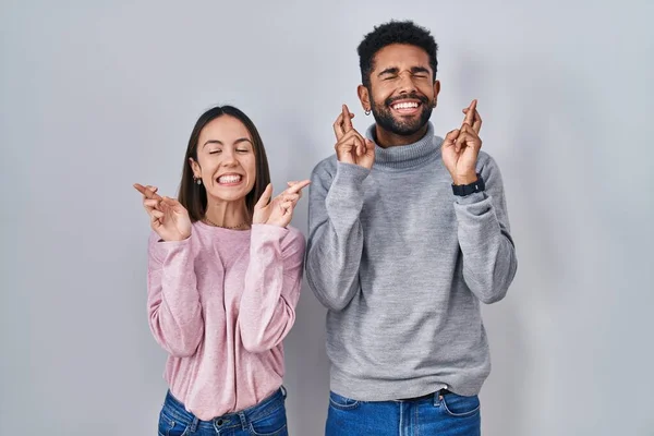 Young Hispanic Couple Standing Together Gesturing Finger Crossed Smiling Hope — Stockfoto