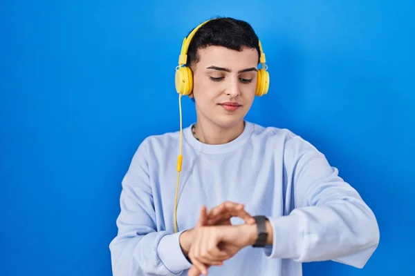 Non binary person listening to music using headphones checking the time on wrist watch, relaxed and confident
