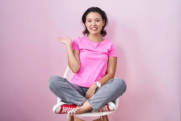 Hispanic Young Woman Sitting Chair Pink Background Smiling Cheerful Presenting — 图库照片