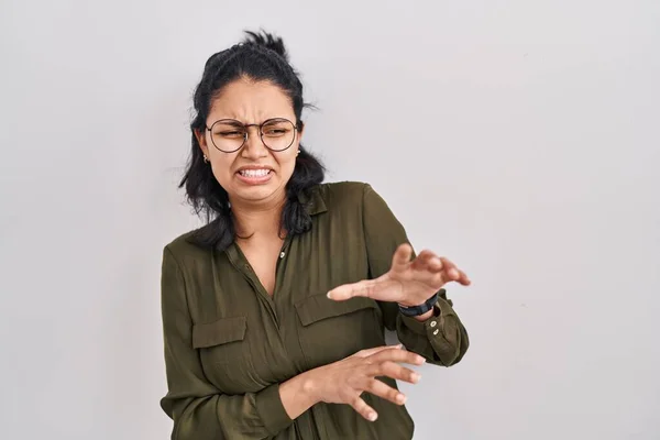 Hispanic woman with dark hair standing over isolated background disgusted expression, displeased and fearful doing disgust face because aversion reaction. with hands raised