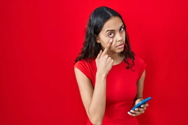 Young Brazilian Woman Using Smartphone Red Background Pointing Eye Watching —  Fotos de Stock