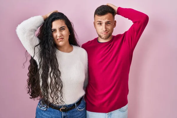 Young Hispanic Couple Standing Pink Background Confuse Wondering Question Uncertain — Stockfoto
