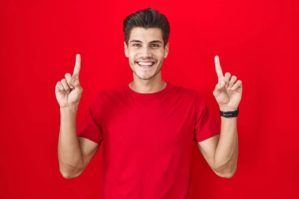 Young Hispanic Man Standing Red Background Smiling Amazed Surprised Pointing — Stockfoto