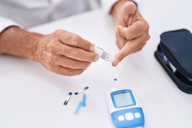 Middle age man measuring glucose sitting on table at home