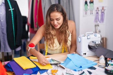 Young beautiful hispanic woman tailor looking color test and cloth at tailor shop