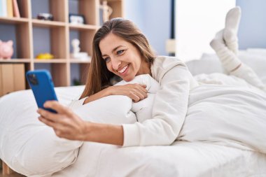 Yatak odasında akıllı telefon kullanan genç bir kadın.